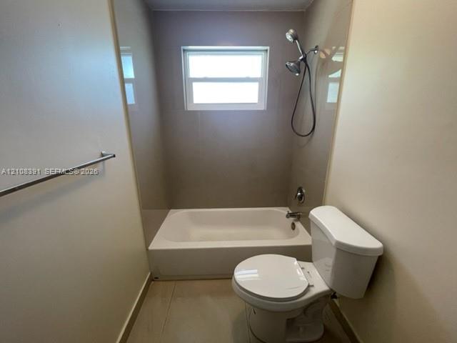 Full bathroom featuring a white porcelain tub and shower combination, wall-mounted handheld shower fixture, single-hung window, and a standard-height toilet