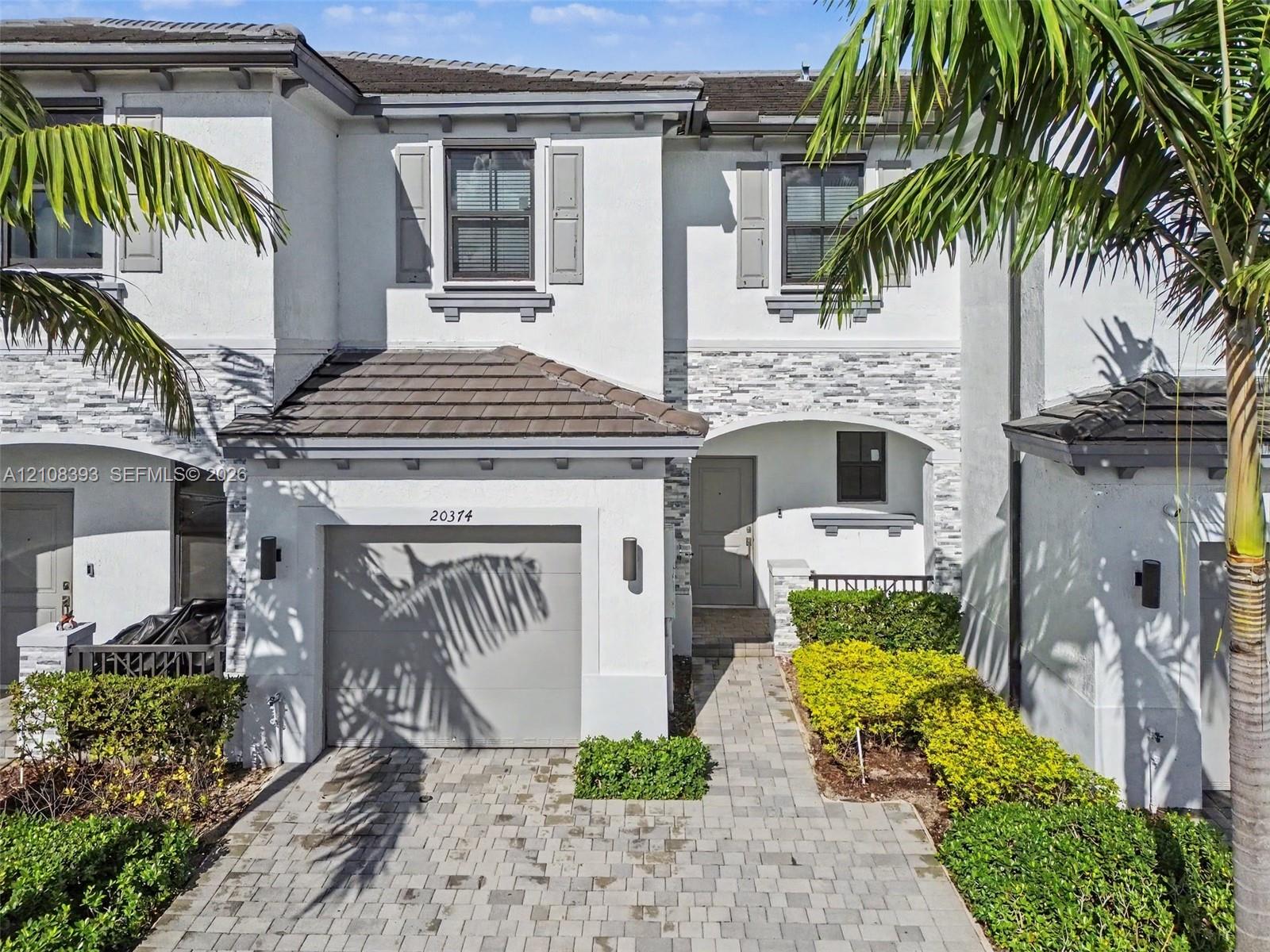 Exterior facade featuring stucco siding, stone veneer accents, concrete tile roofing, shutters, and a paver driveway