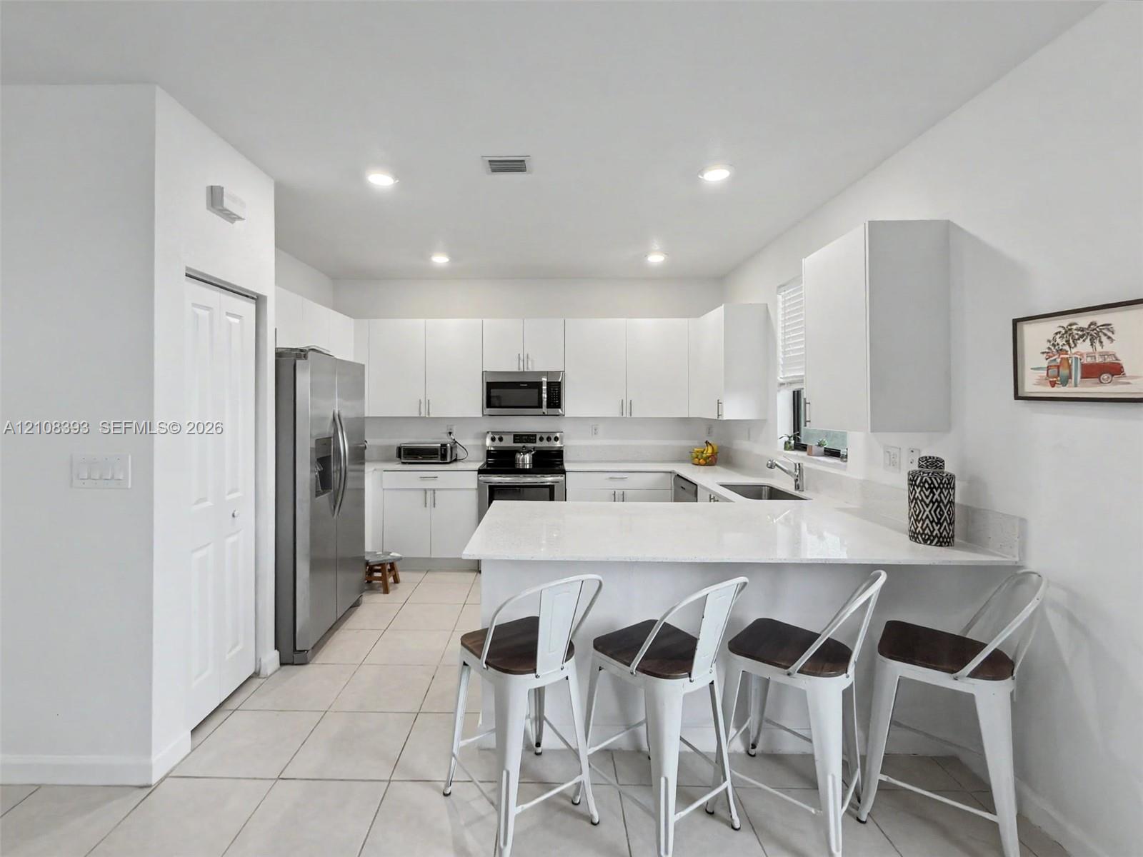 Kitchen featuring white cabinetry, solid-surface countertops with a breakfast bar, recessed ceiling lighting, stainless steel appliances, and tile flooring