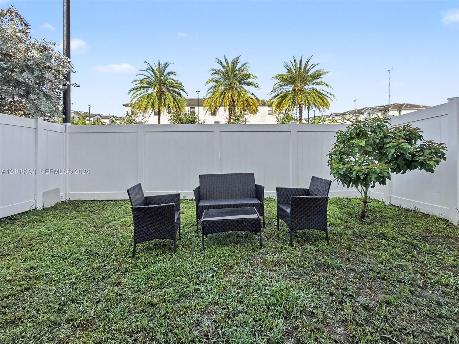 Enclosed backyard featuring white vinyl privacy fencing and a mature tree