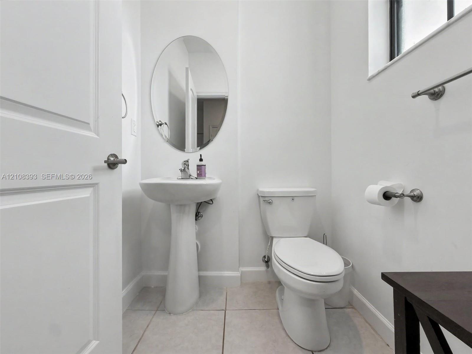 Pedestal sink, oval wall mirror, ceramic tile flooring, and a two-piece toilet