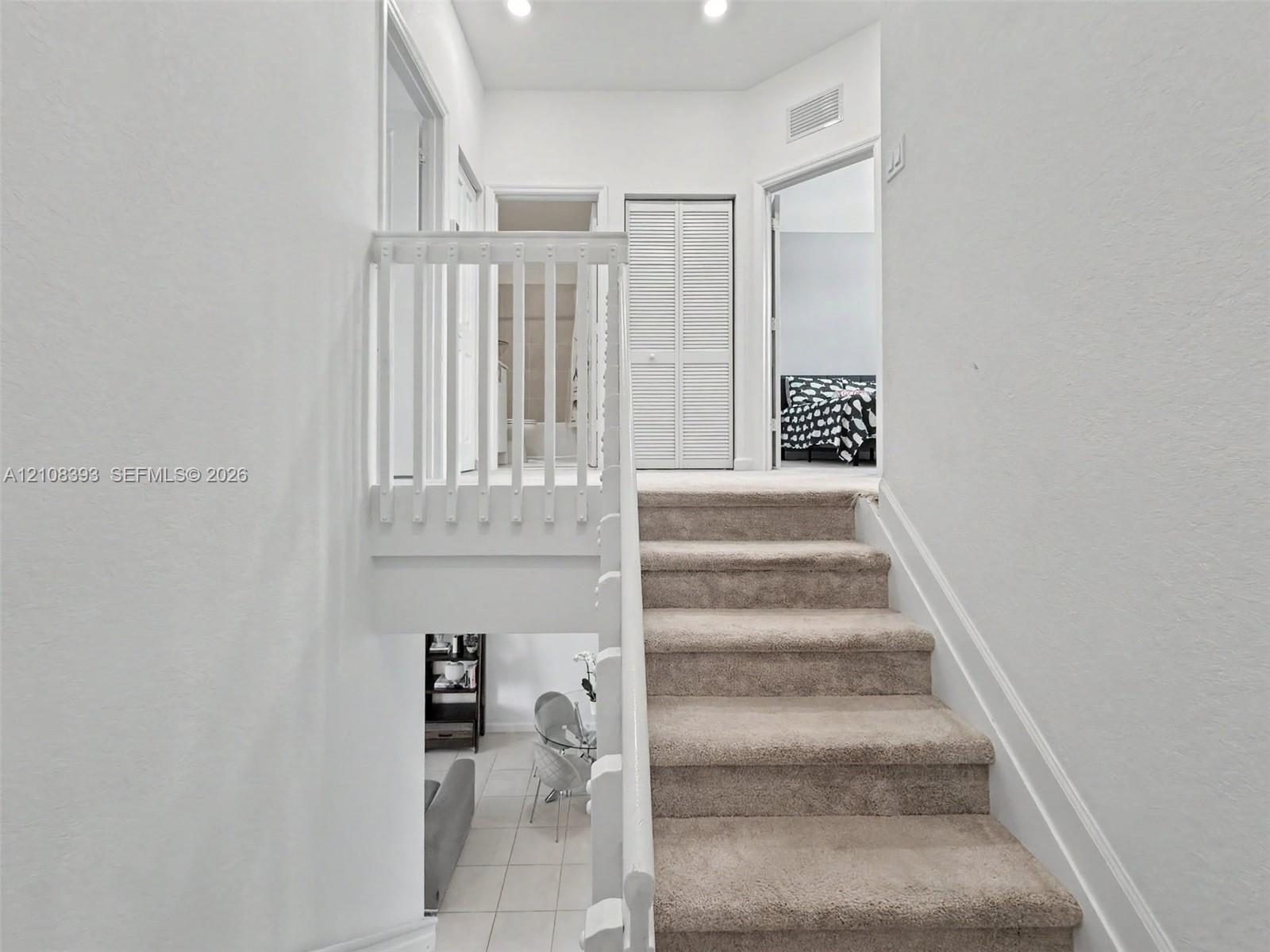 Staircase featuring neutral carpeting, white wooden balustrades, recessed ceiling lighting, and louvered closet doors