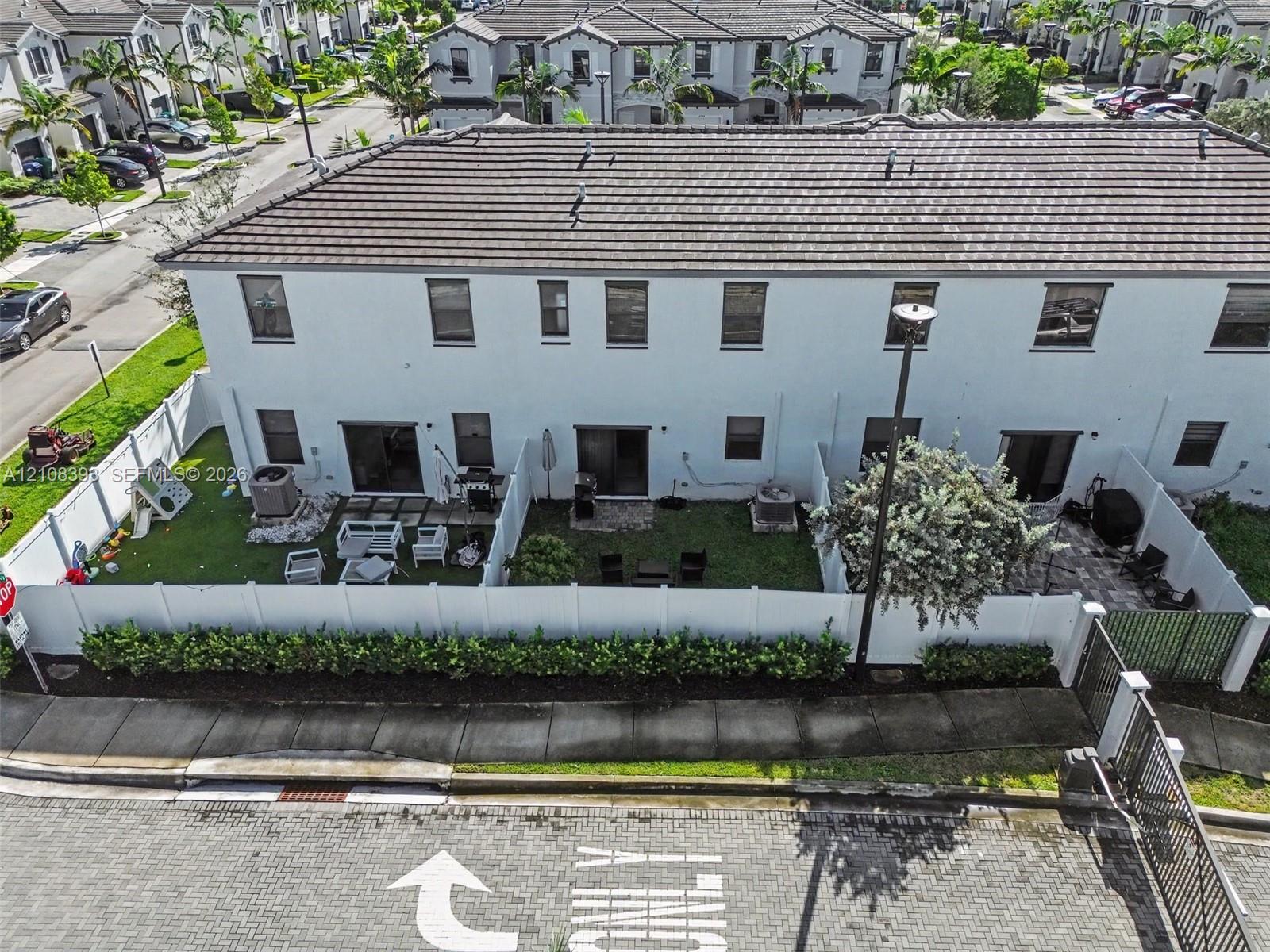 Two-story townhouse exterior featuring white stucco siding, a tiled roof, private fenced rear yards with patio pavers, and manicured landscaping