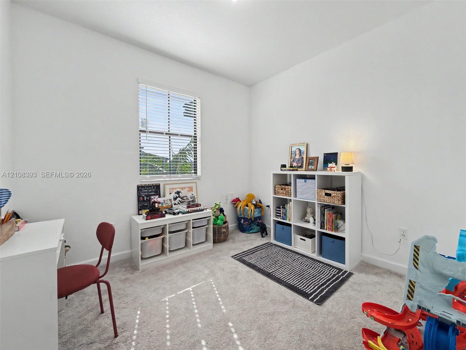 Neutral-toned carpeting, crisp white walls, and a large window with horizontal blinds