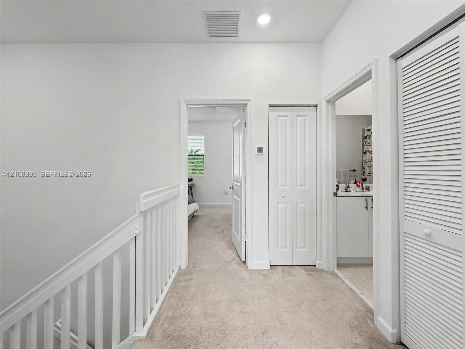 Hallway featuring neutral carpeting, white interior doors, a louvered closet door, and a white balustrade railing