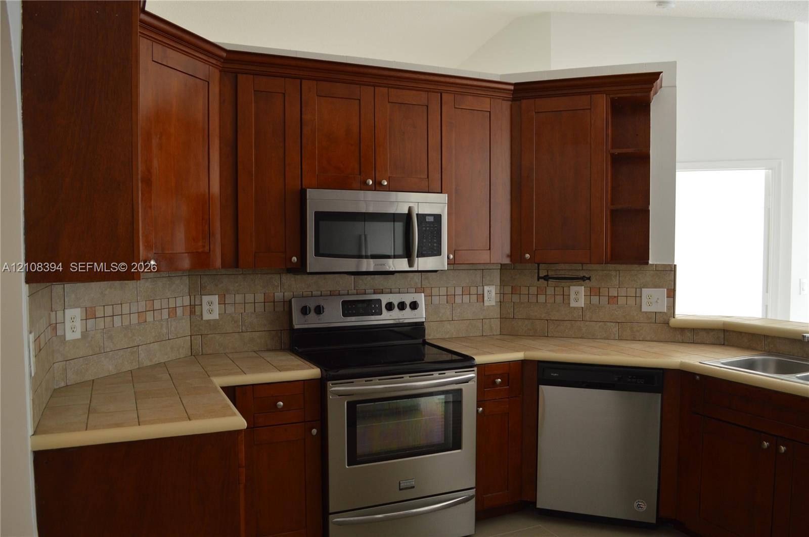Kitchen featuring wood cabinetry, tiled countertops, stainless steel appliances, and a decorative tile backsplash Kitchen featuring wood cabinetry, tiled countertops, stainless steel appliances, and a decorative tile backsplash