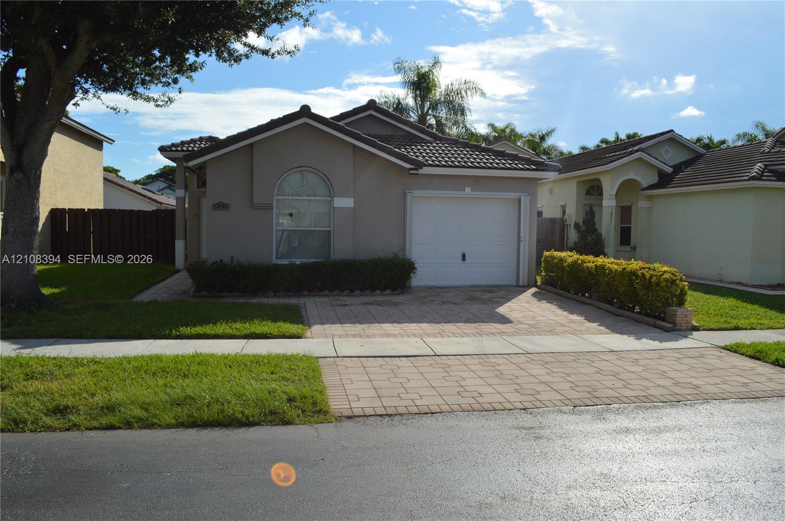 Single-story residence featuring a tile roof, neutral stucco exterior, arched window detail, and an attached garage with a paved driveway Single-story residence featuring a tile roof, neutral stucco exterior, arched window detail, and an attached garage with a paved driveway