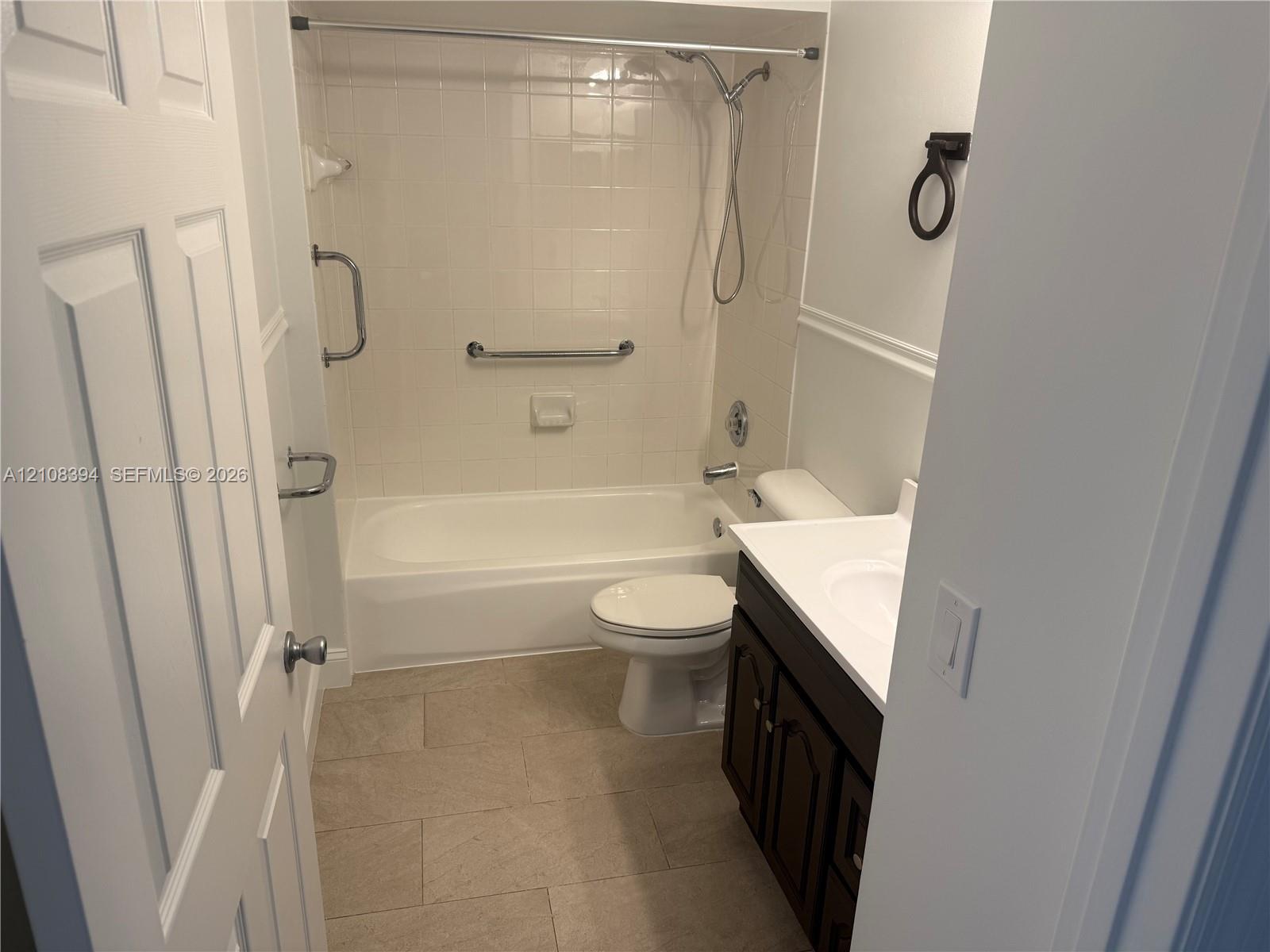 Bathroom featuring a deep-basin tub with a tiled surround, a dark wood-finish vanity with a white countertop, and stone-tile flooring Bathroom featuring a deep-basin tub with a tiled surround, a dark wood-finish vanity with a white countertop, and stone-tile flooring