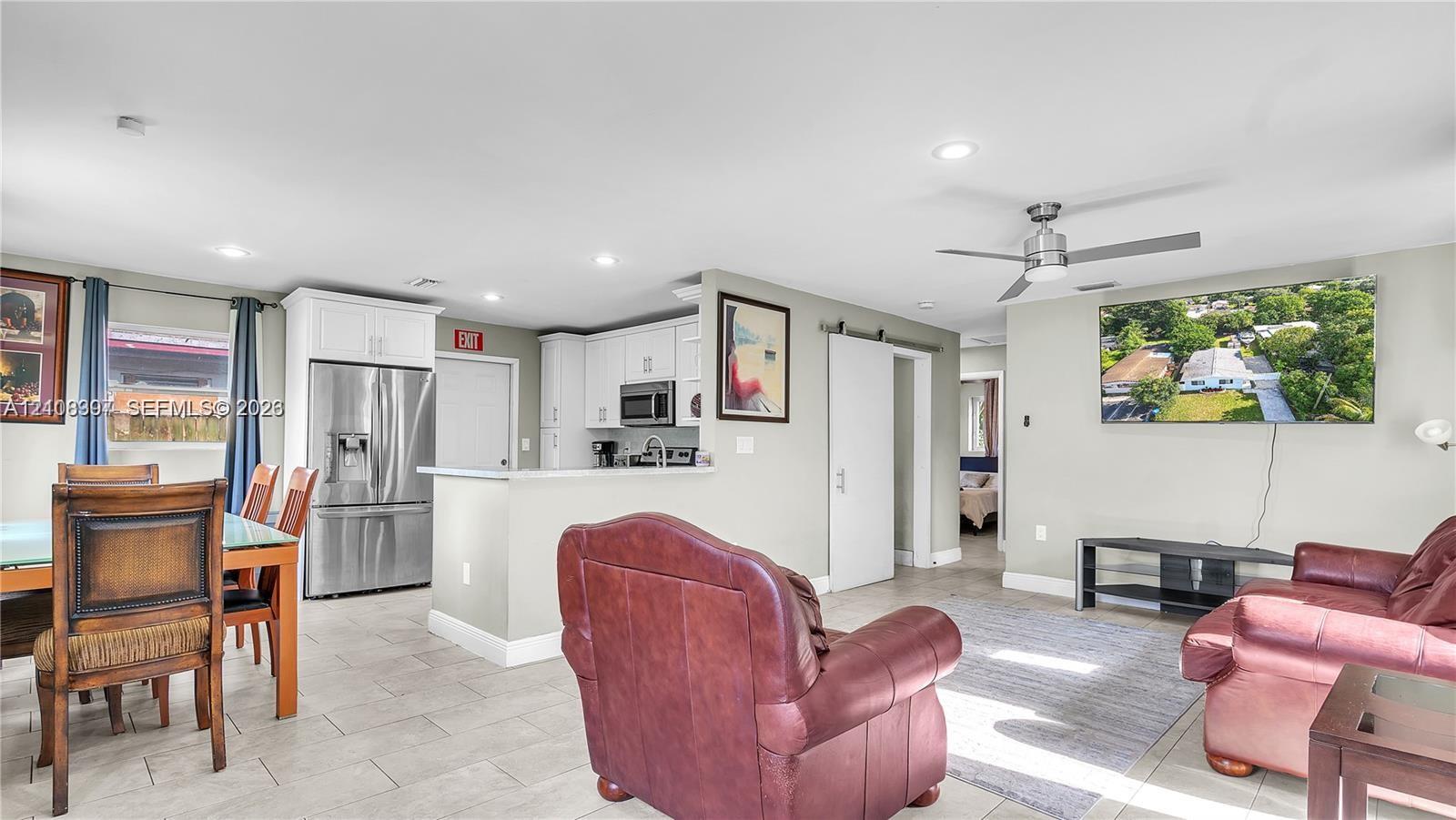 Open-concept floor plan featuring light-toned tile flooring, recessed lighting, white cabinetry, stainless steel refrigerator, and a sliding barn door