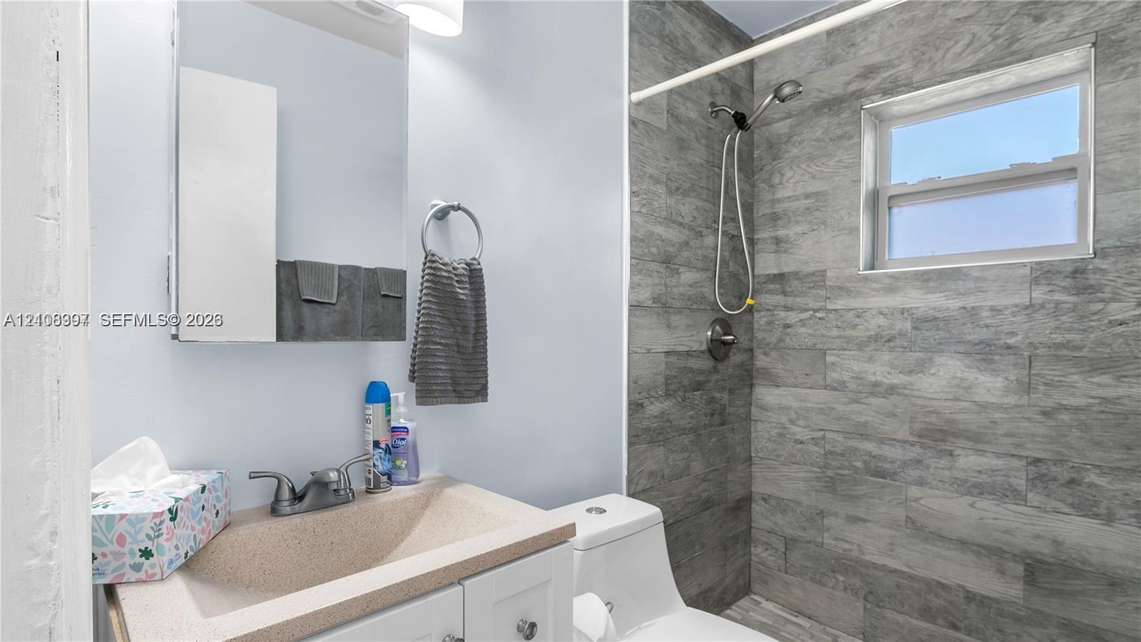 Bathroom featuring a vanity with integrated sink, wall-mounted medicine cabinet, shower area with wood-finish tile surround, and a single-hung window