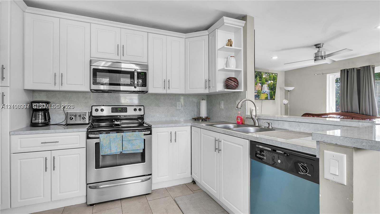 Kitchen featuring white shaker-style cabinetry, stainless steel appliances, a stone-composite countertop, and an undermount dual-basin sink with a gooseneck faucet