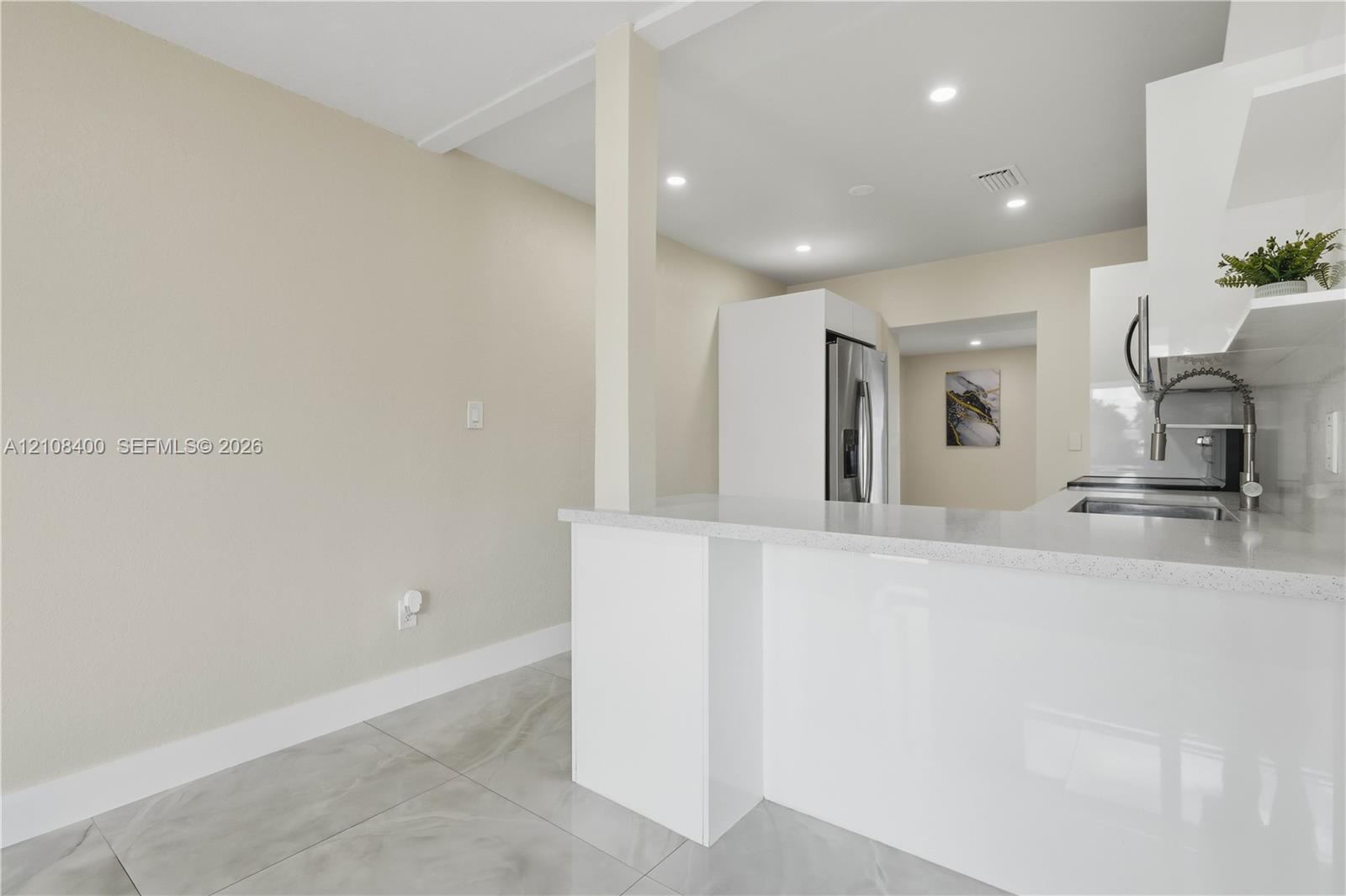 Kitchen featuring white cabinetry, quartz countertops, a stainless steel undermount sink with a gooseneck faucet, large-format tile flooring, and recessed ceiling lighting