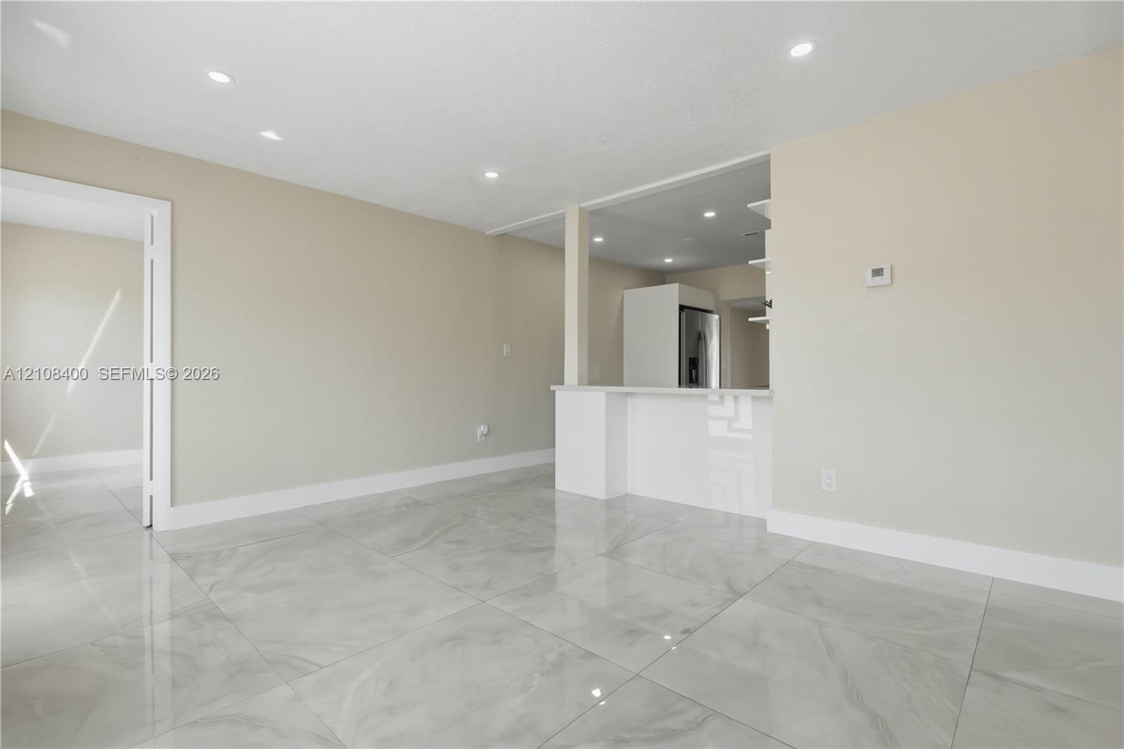 Large-format tile flooring, neutral wall tones, recessed lighting, and a breakfast bar with stone-surfaced countertop