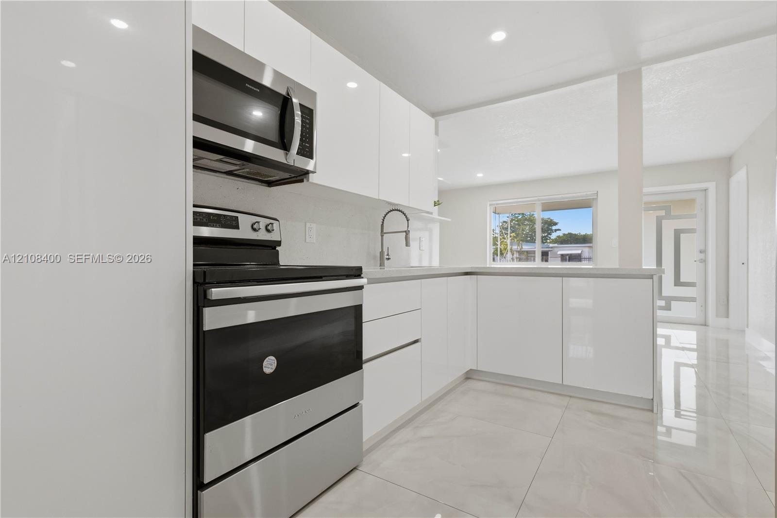 Kitchen featuring high-gloss white cabinetry, stainless steel appliances, neutral stone-finish flooring, and recessed lighting Kitchen featuring high-gloss white cabinetry, stainless steel appliances, neutral stone-finish flooring, and recessed lighting