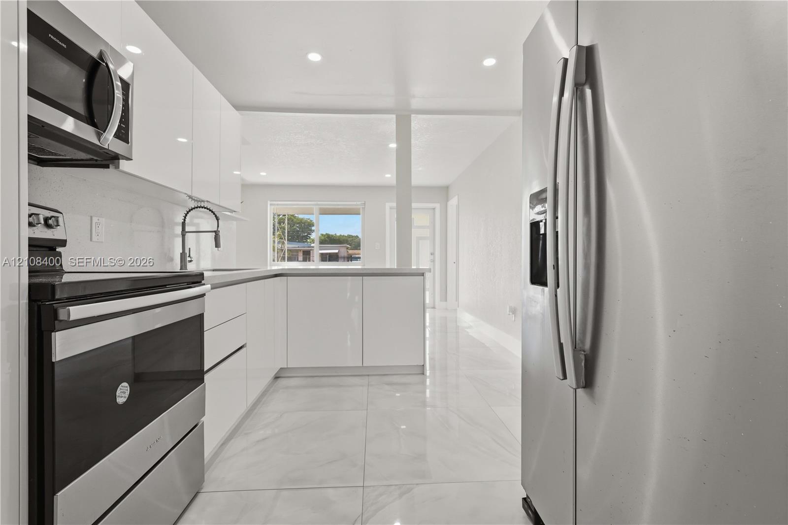 Kitchen featuring high-gloss white cabinetry, stainless steel appliances, recessed lighting, and large-format tile flooring Kitchen featuring high-gloss white cabinetry, stainless steel appliances, recessed lighting, and large-format tile flooring