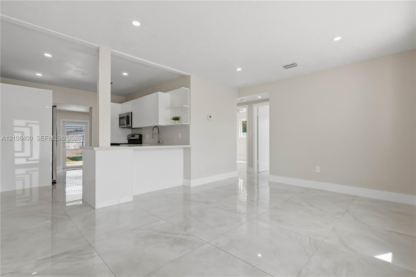 Open-concept interior featuring large-format tile flooring, white cabinetry, integrated peninsula, and recessed lighting Open-concept interior featuring large-format tile flooring, white cabinetry, integrated peninsula, and recessed lighting