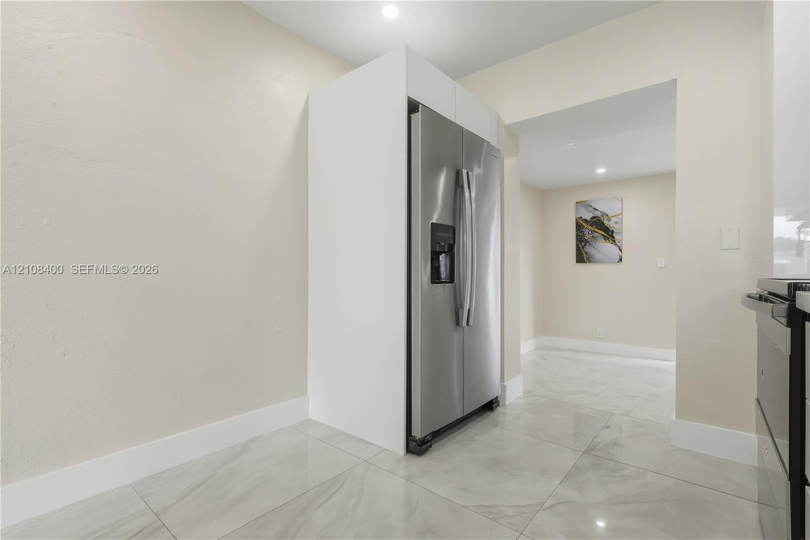 Stainless steel side-by-side refrigerator, white built-in cabinetry surround, and large-format tile flooring