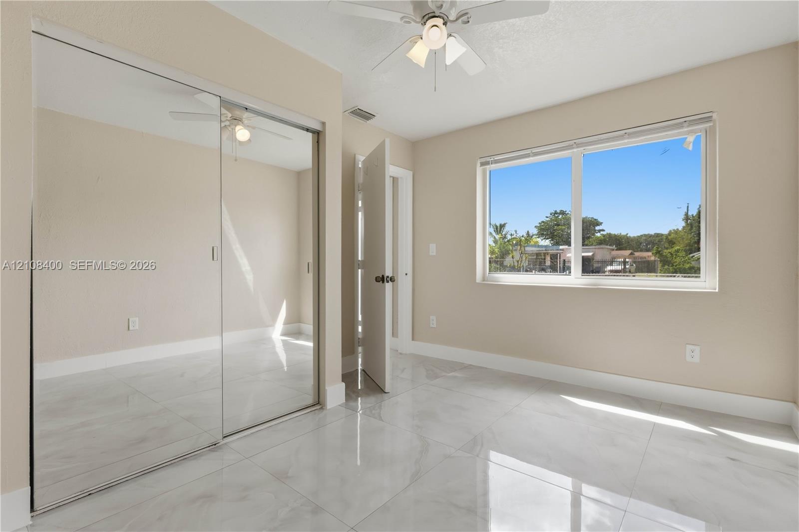 Room with high-gloss polished tile flooring, mirrored sliding closet doors, a neutral color palette, a multi-light ceiling fan, and a large horizontal window Room with high-gloss polished tile flooring, mirrored sliding closet doors, a neutral color palette, a multi-light ceiling fan, and a large horizontal window