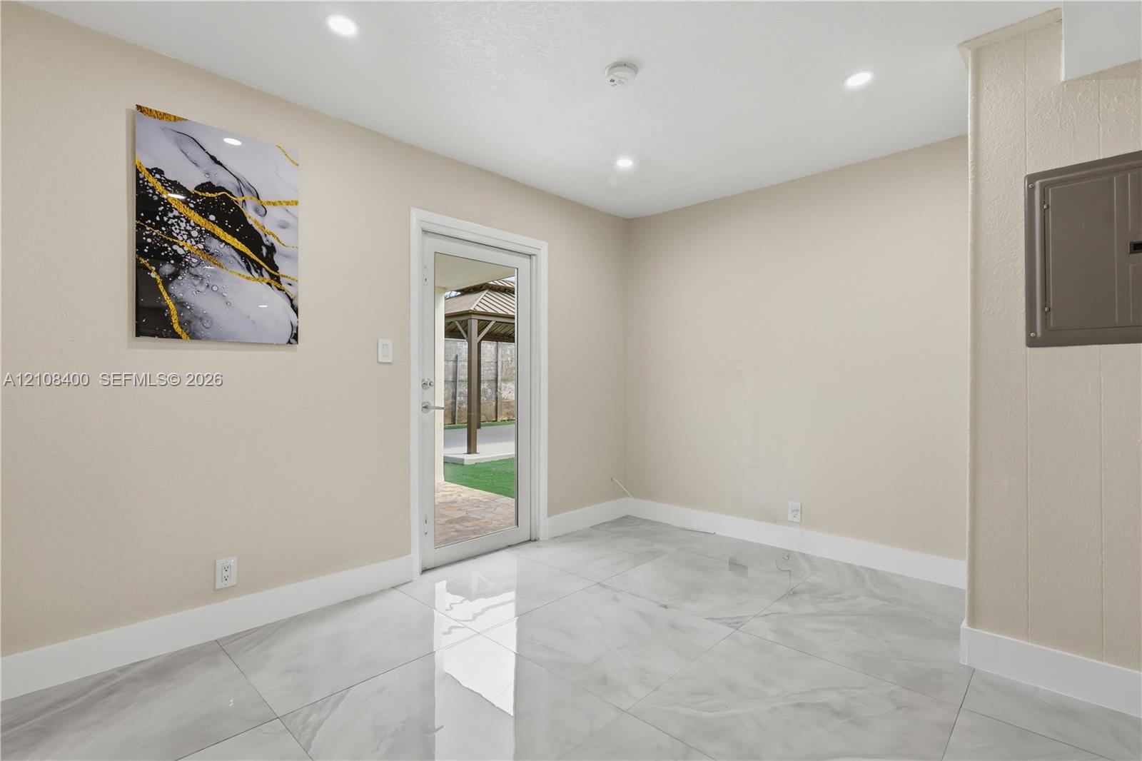 Neutral-toned interior space featuring large-format stone-finish tile flooring, recessed ceiling lighting, and a glass-paneled exterior door