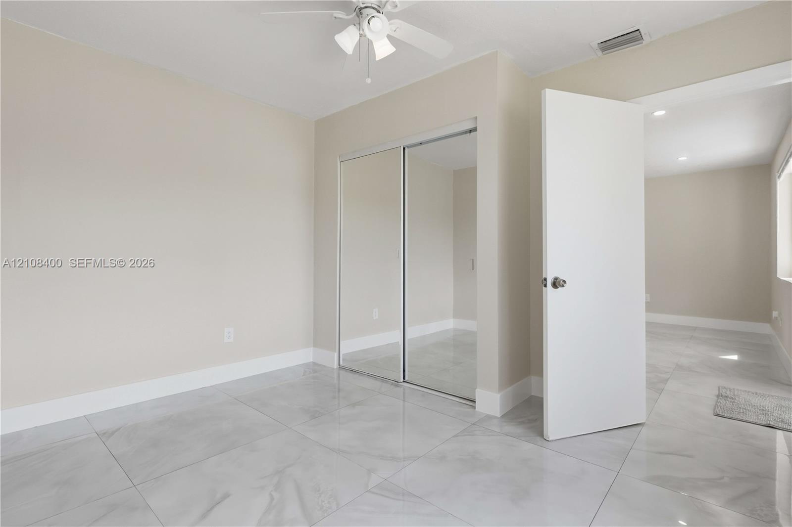 Room featuring large-format tile flooring, sliding mirrored closet doors, and a ceiling fan with integrated lighting