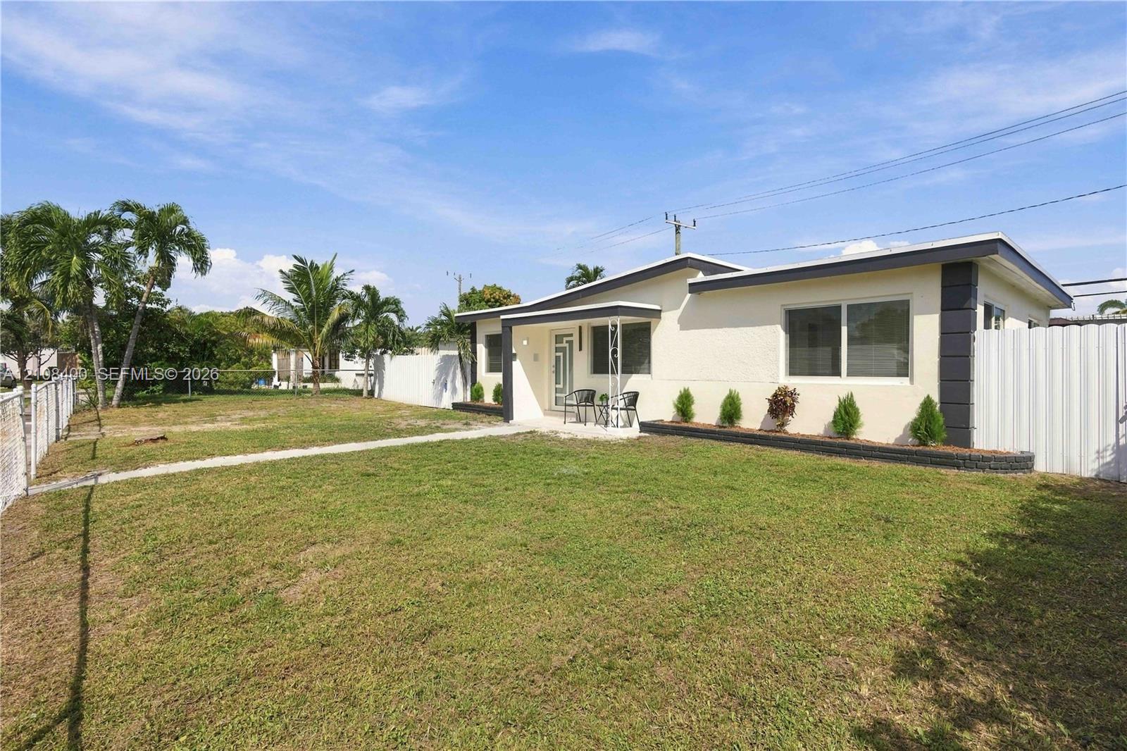 Single-story exterior featuring a light-toned textured facade, horizontal sliding windows, metal-post entryway canopy, and a fenced yard with perimeter landscaping Single-story exterior featuring a light-toned textured facade, horizontal sliding windows, metal-post entryway canopy, and a fenced yard with perimeter landscaping