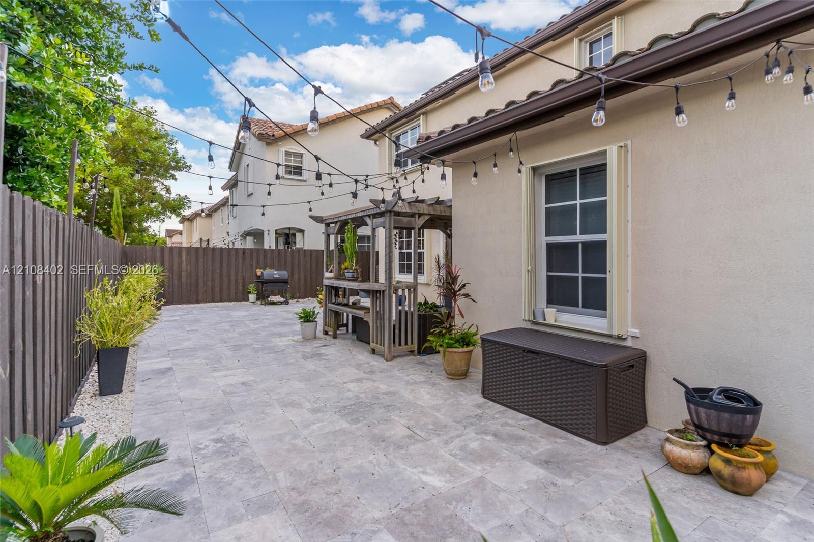 Paved patio featuring stone tile surfacing, wood-slat perimeter fencing, a built-in wooden pergola, and overhead string lighting