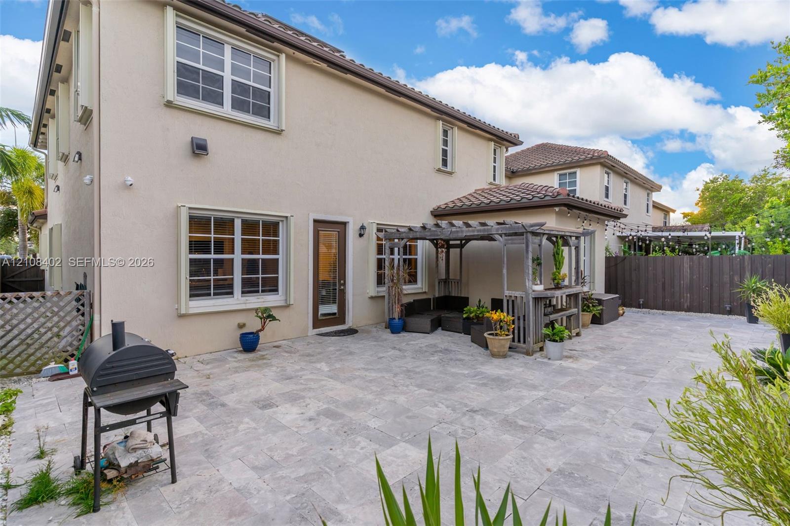 Stucco exterior featuring a paved stone patio, custom wood pergola, multi-pane windows, and tile roof