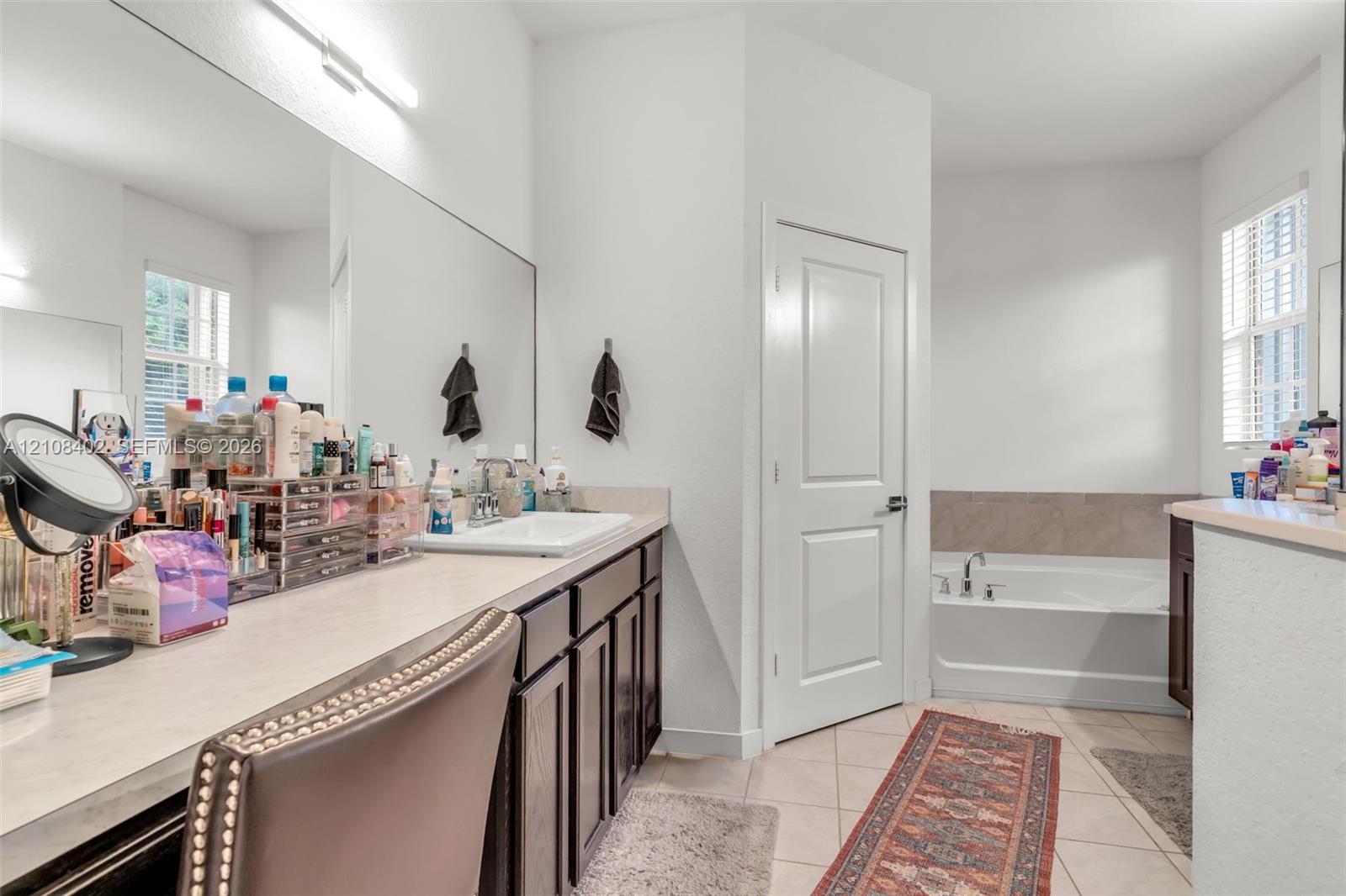 Bathroom featuring an expansive vanity with dark-finish cabinetry, a large wall-to-wall mirror, a rectangular drop-in sink, and a separate soaking tub with tiled surround
