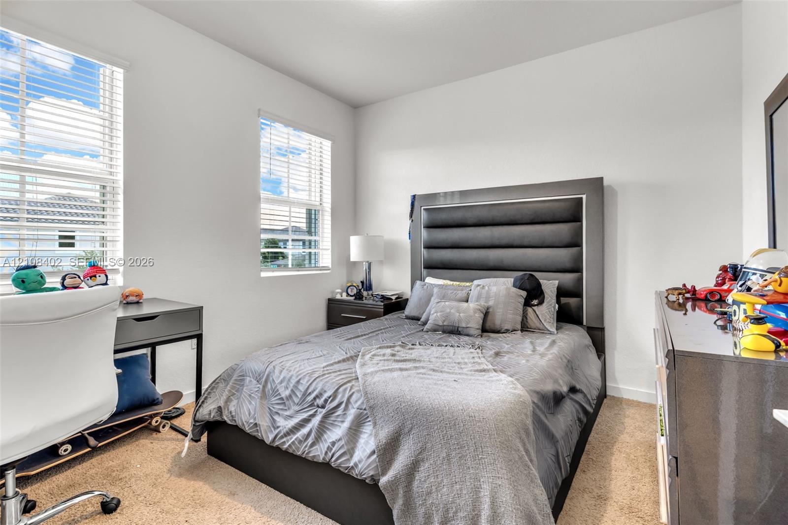 Neutral-toned bedroom featuring plush carpeting, dual-pane windows with horizontal blinds, and smooth-finish white walls