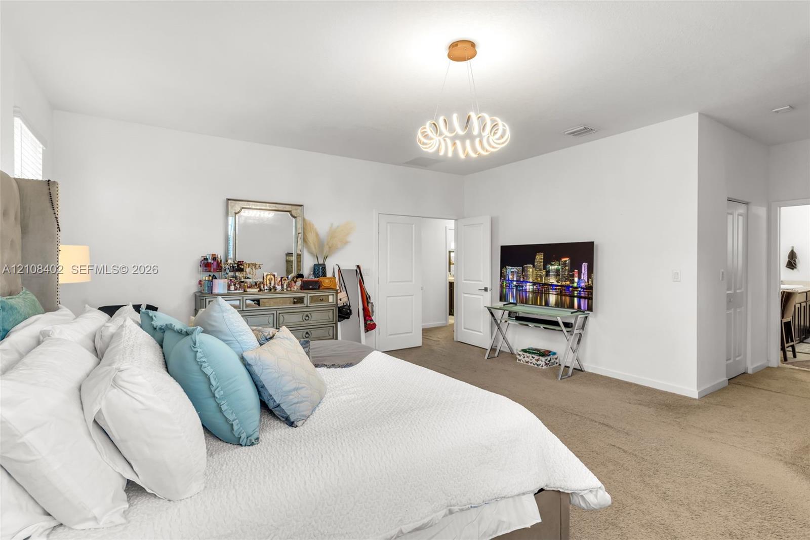 Neutral-toned wall-to-wall carpeting, modern circular spiral-design chandelier, two-panel interior doors, and crisp white wall finish
