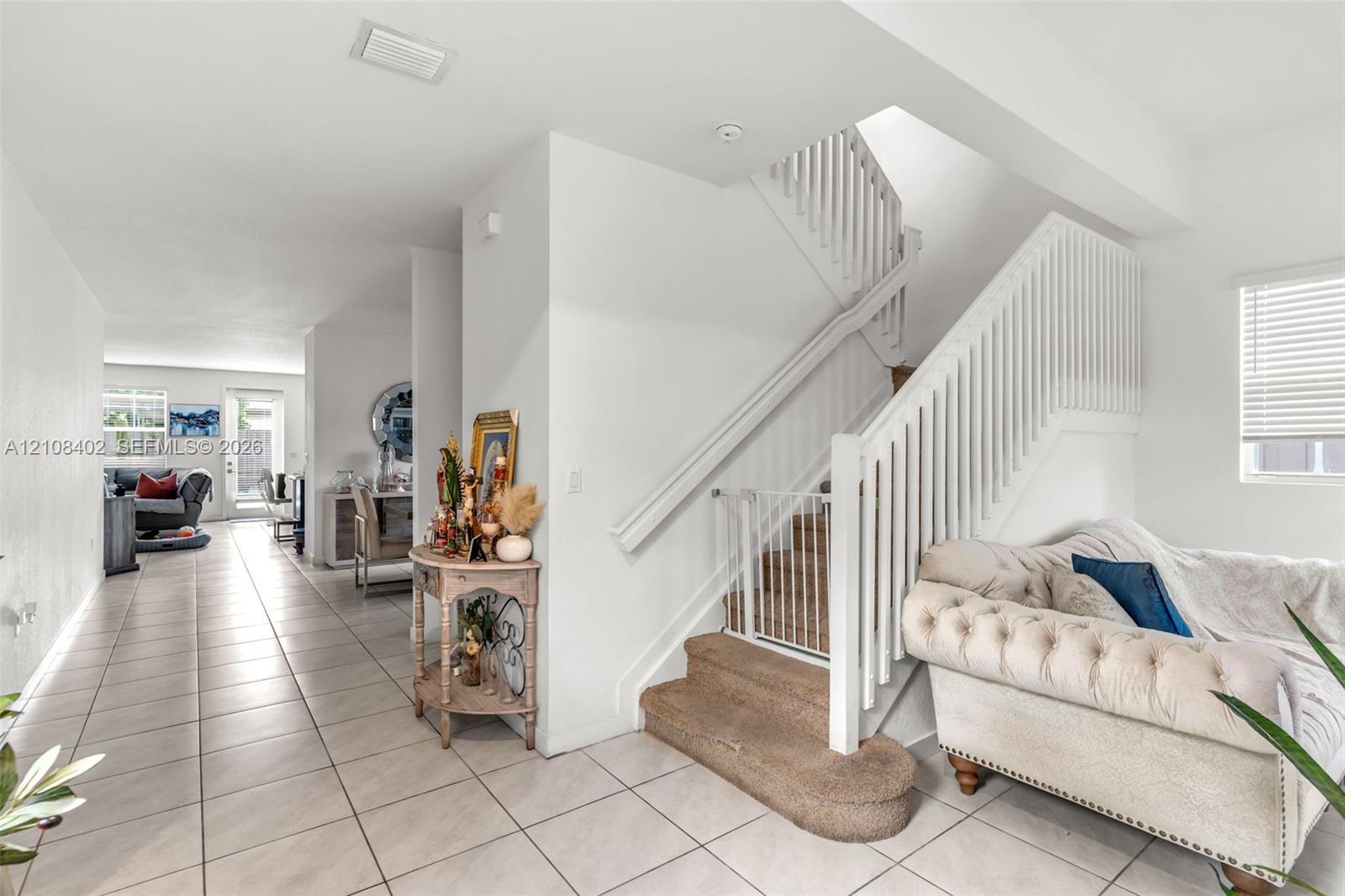 Staircase featuring white balusters and a carpeted tread, complemented by neutral-toned floor tile throughout