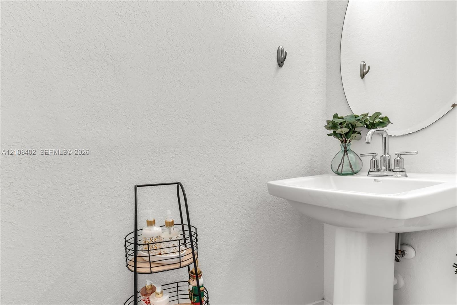 Pedestal sink featuring a polished chrome faucet and a circular wall-mounted mirror
