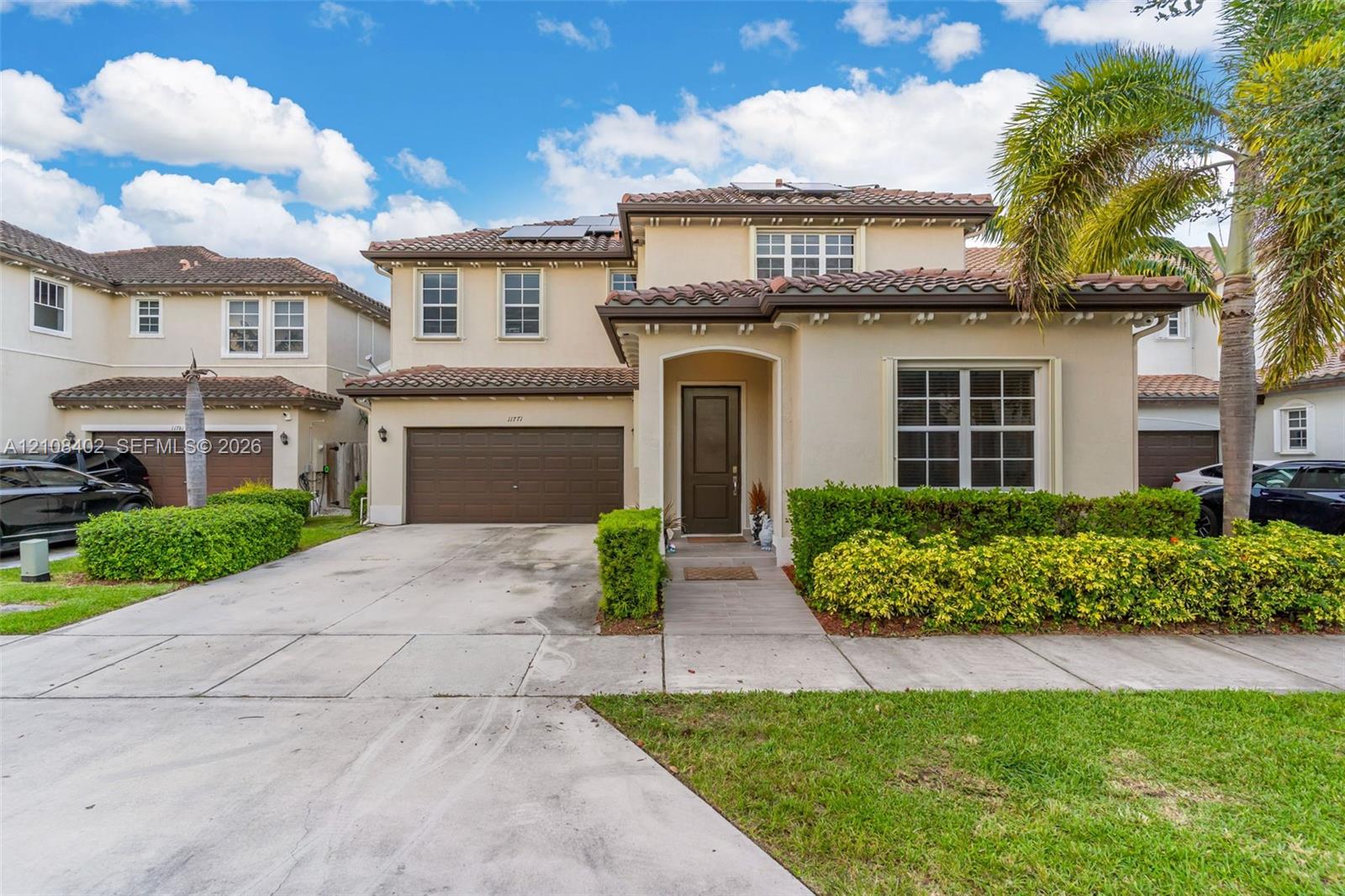 Stucco exterior featuring a clay tile roof, arched entryway, multi-panel garage door, and solar panels
