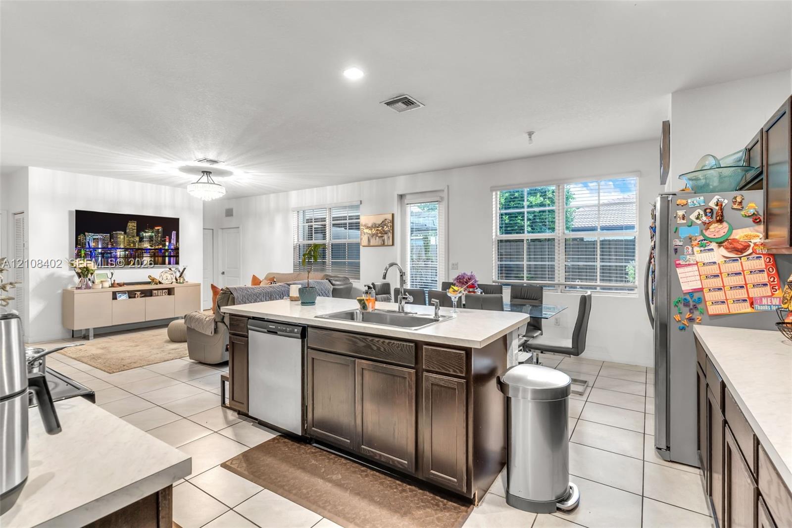 Kitchen featuring a central island with a stainless steel undermount sink, dark wood-finish cabinetry, solid-surface countertops, tile flooring, and stainless steel appliances