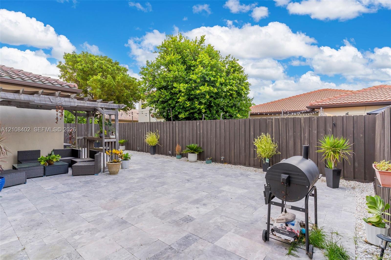 Outdoor living area featuring a neutral-toned stone paver patio, a wooden pergola, and a full-height privacy fence