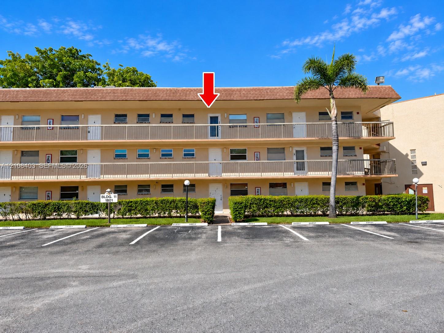 Three-story multi-unit building featuring a textured stucco facade, metal-railing balconies, a low-pitch shingle roof, and exterior landscaping