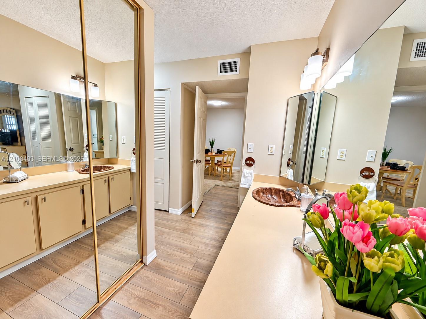 Located in the Master bathroom- Dual-sink vanity area with custom-fitted mirror panels, solid surface countertops, textured copper-finish vessel sinks, and wood-finish flooring Located in the Master bathroom- Dual-sink vanity area with custom-fitted mirror panels, solid surface countertops, textured copper-finish vessel sinks, and wood-finish flooring