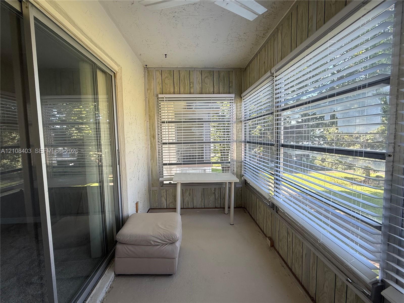 Enclosed sunroom featuring vertical wood paneling, sliding glass door entry, ceiling fan, and large windows with horizontal blinds