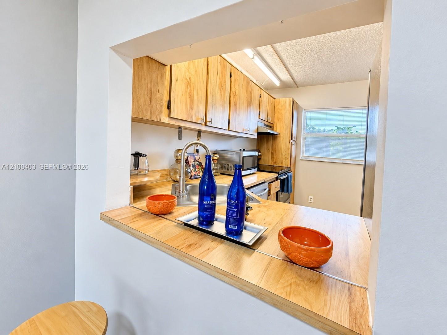 Kitchen pass-through window featuring a wood-finish countertop, stainless steel sink, gooseneck faucet, and light wood cabinetry Kitchen pass-through window featuring a wood-finish countertop, stainless steel sink, gooseneck faucet, and light wood cabinetry
