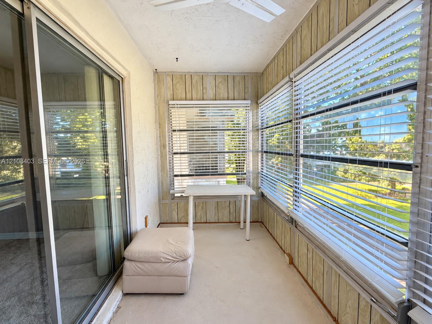 Enclosed sunroom featuring vertical wood paneling, floor-to-ceiling windows with horizontal blinds, sliding glass door entry, and a ceiling-mounted fan