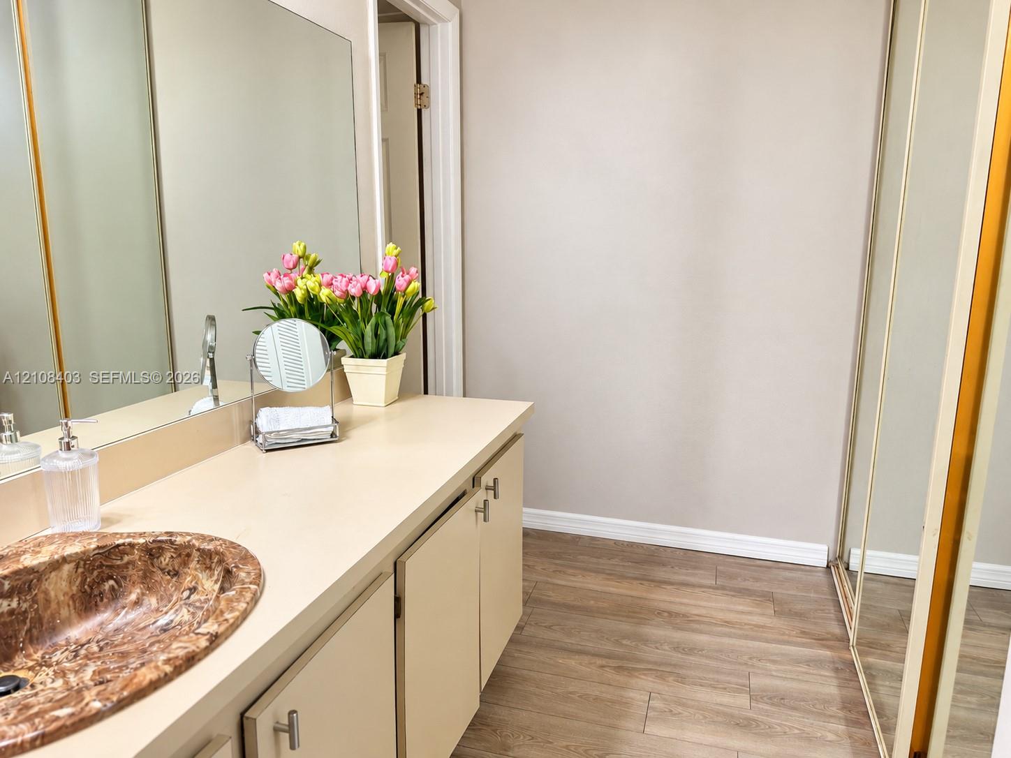 Master Bathroom vanity featuring a solid surface countertop, an oval inset stone-finish sink, extensive wall-spanning mirror, and wood-finish flooring Master Bathroom vanity featuring a solid surface countertop, an oval inset stone-finish sink, extensive wall-spanning mirror, and wood-finish flooring