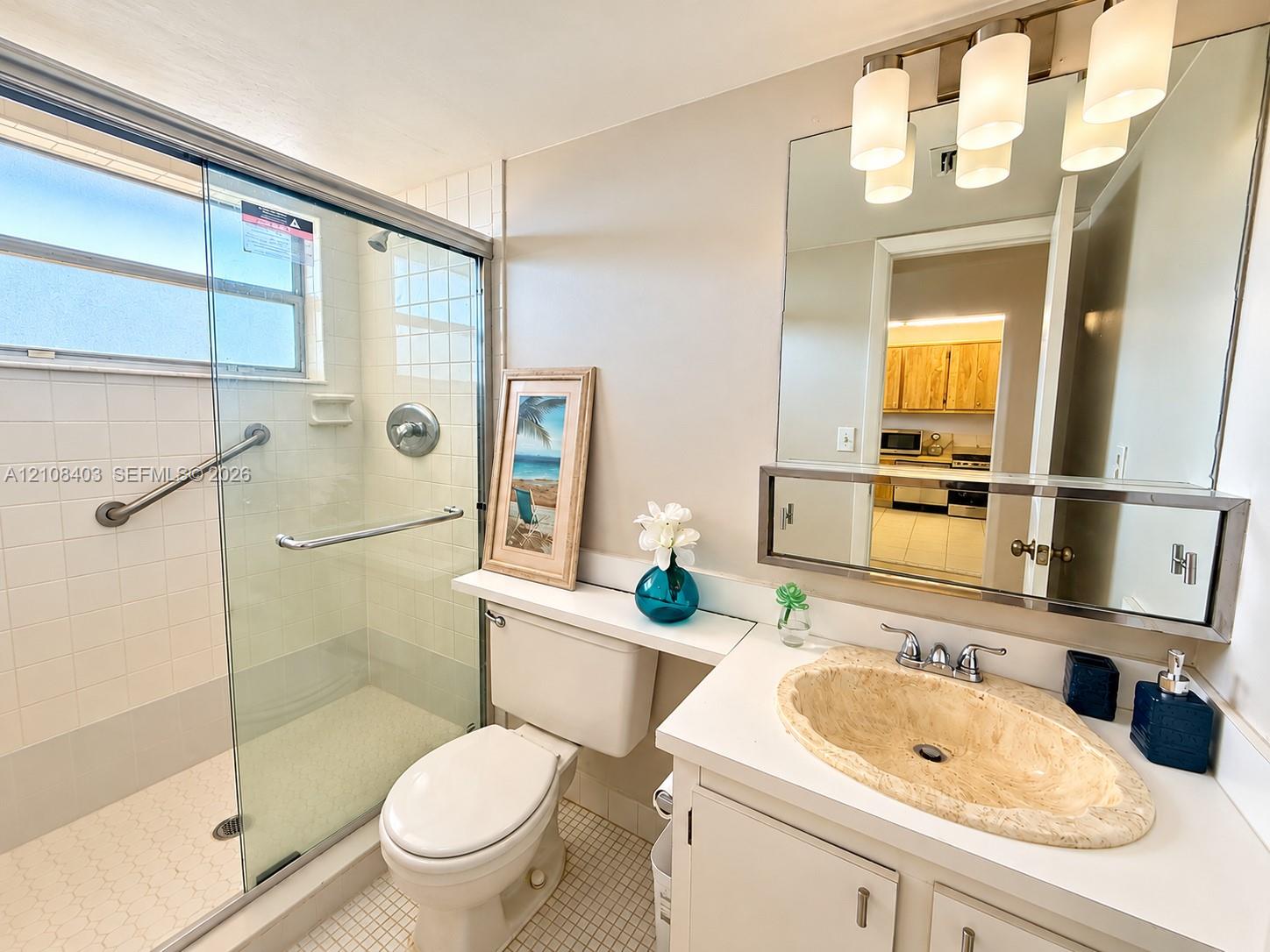 Bathroom featuring a glass-enclosed shower with tile surround, vanity with a stone-finish oval sink, and a large wall-mounted mirror with integrated lighting Bathroom featuring a glass-enclosed shower with tile surround, vanity with a stone-finish oval sink, and a large wall-mounted mirror with integrated lighting