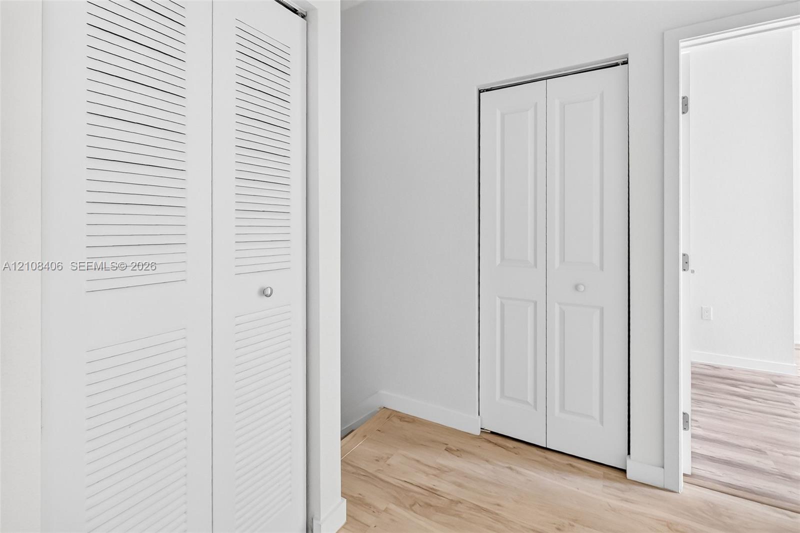 White bi-fold doors with louvered panels, white paneled doors, and light-toned wood-finish flooring