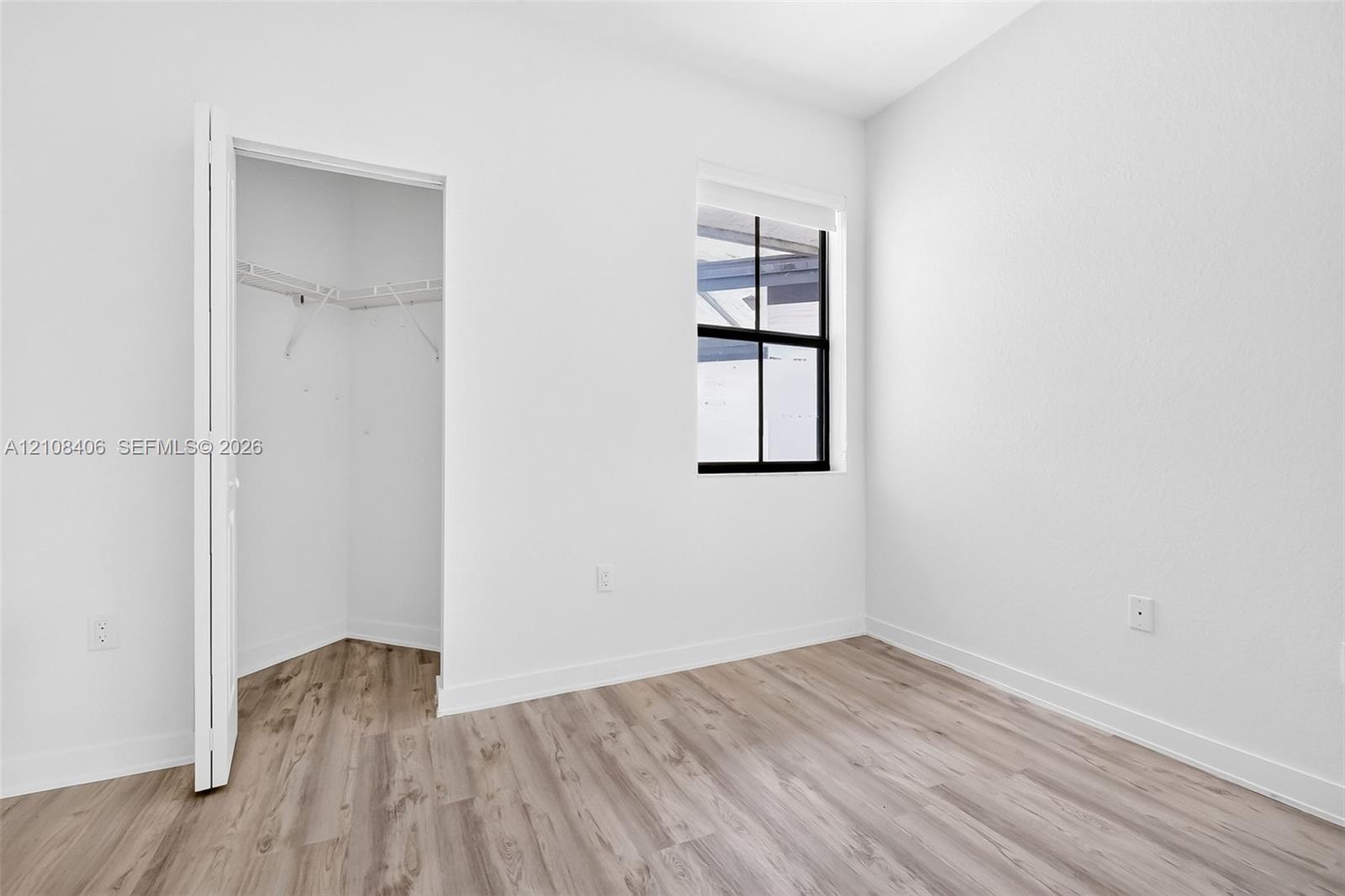 Neutral interior featuring wood-finish flooring, a black-framed window, and a walk-in closet with built-in wire shelving