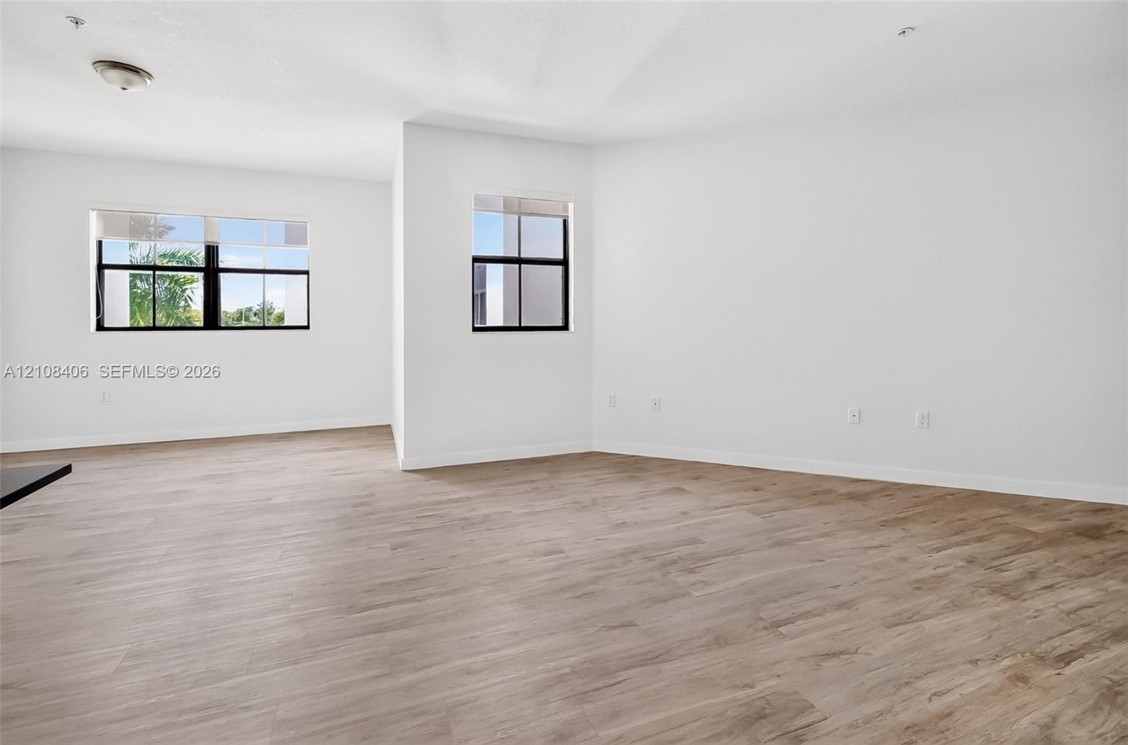 Neutral-toned wood-finish flooring, two large windows with black frames, and recessed lighting fixtures