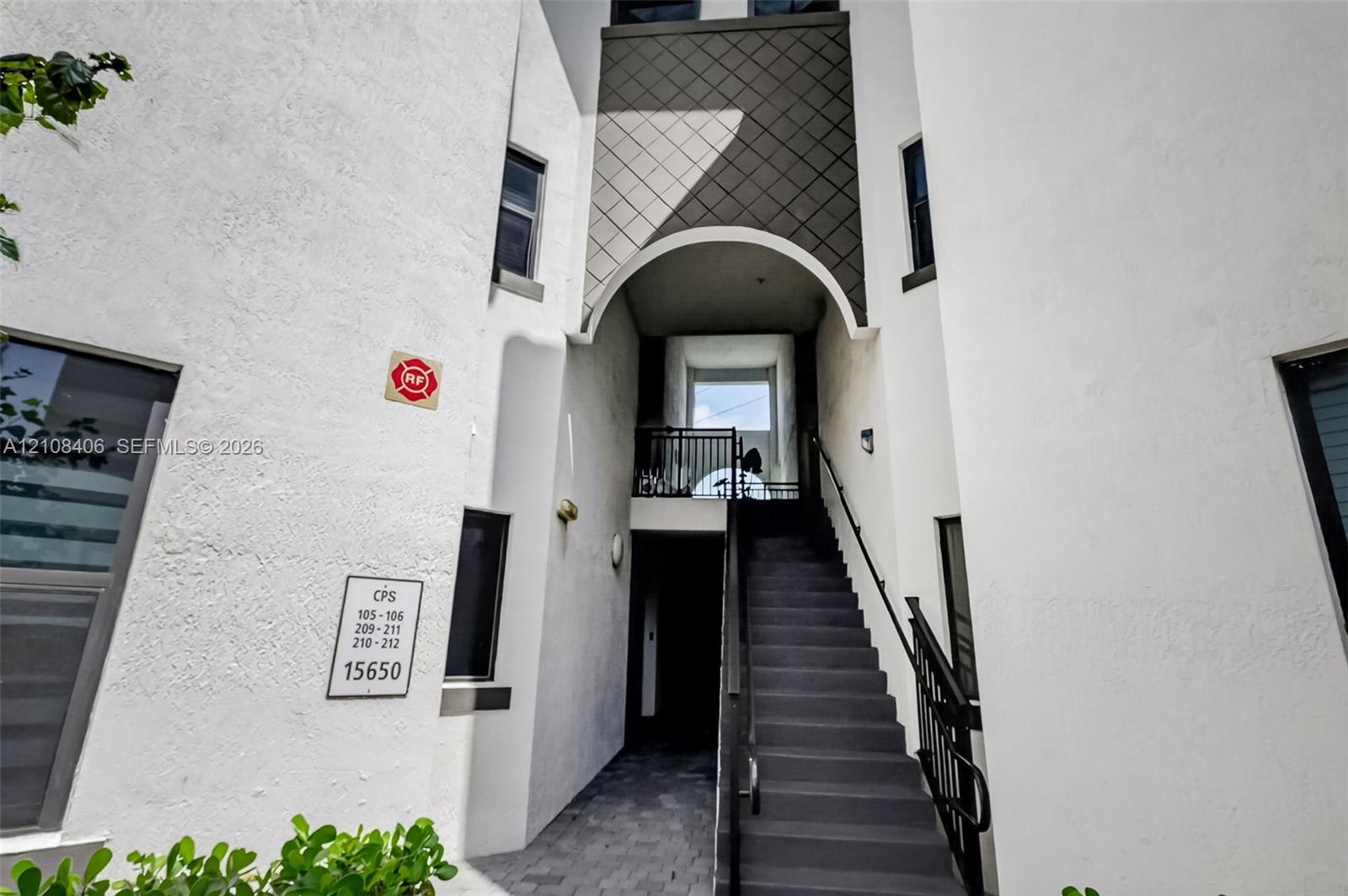 Stucco exterior featuring an arched entryway, diamond-patterned siding accents, and a metal staircase with a black handrail