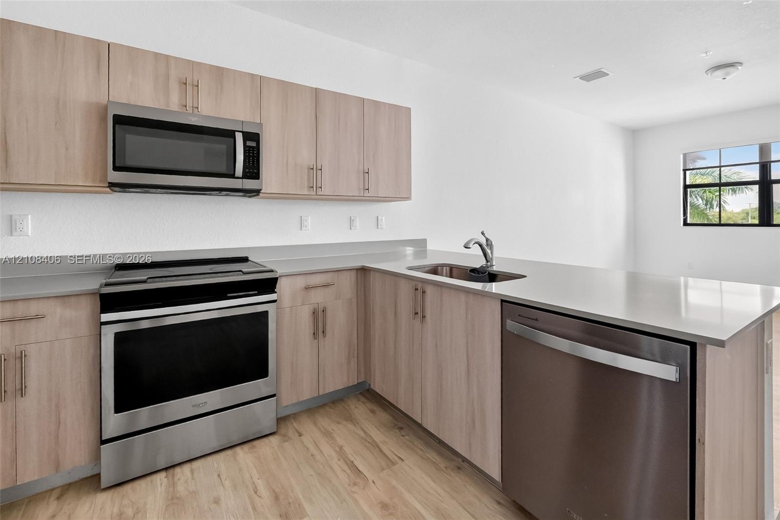 Kitchen featuring light-tone flat-panel cabinetry, stainless steel appliances, solid-surface countertops, an undermount sink with a pull-down faucet, and wood-finish flooring
