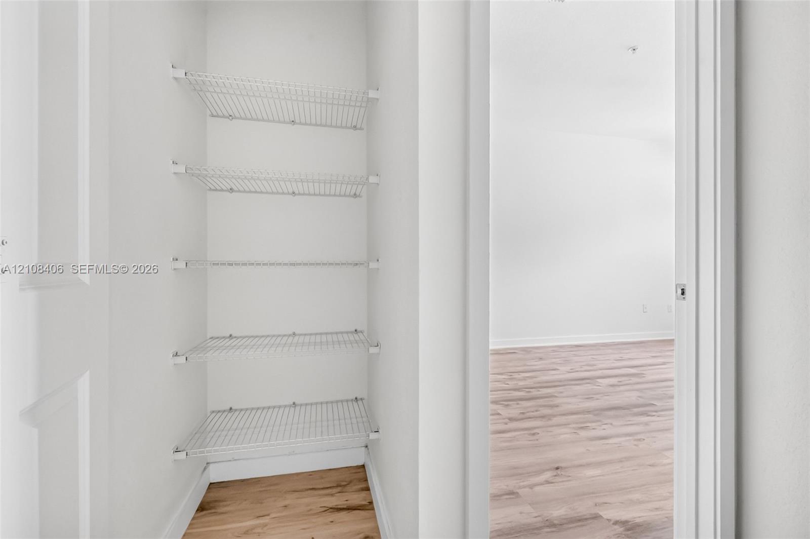 Storage closet featuring five tiers of white wire shelving and wood-finish flooring
