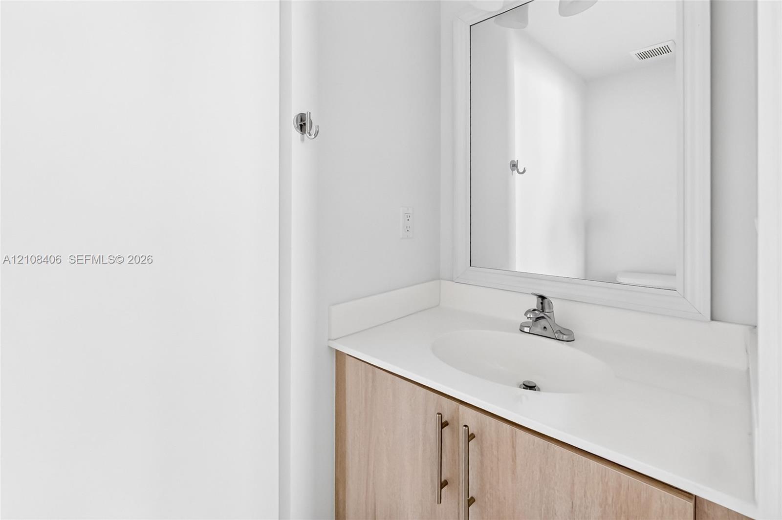 Wood-finish vanity cabinet with metallic hardware, integrated white countertop, oval basin, and a framed mirror