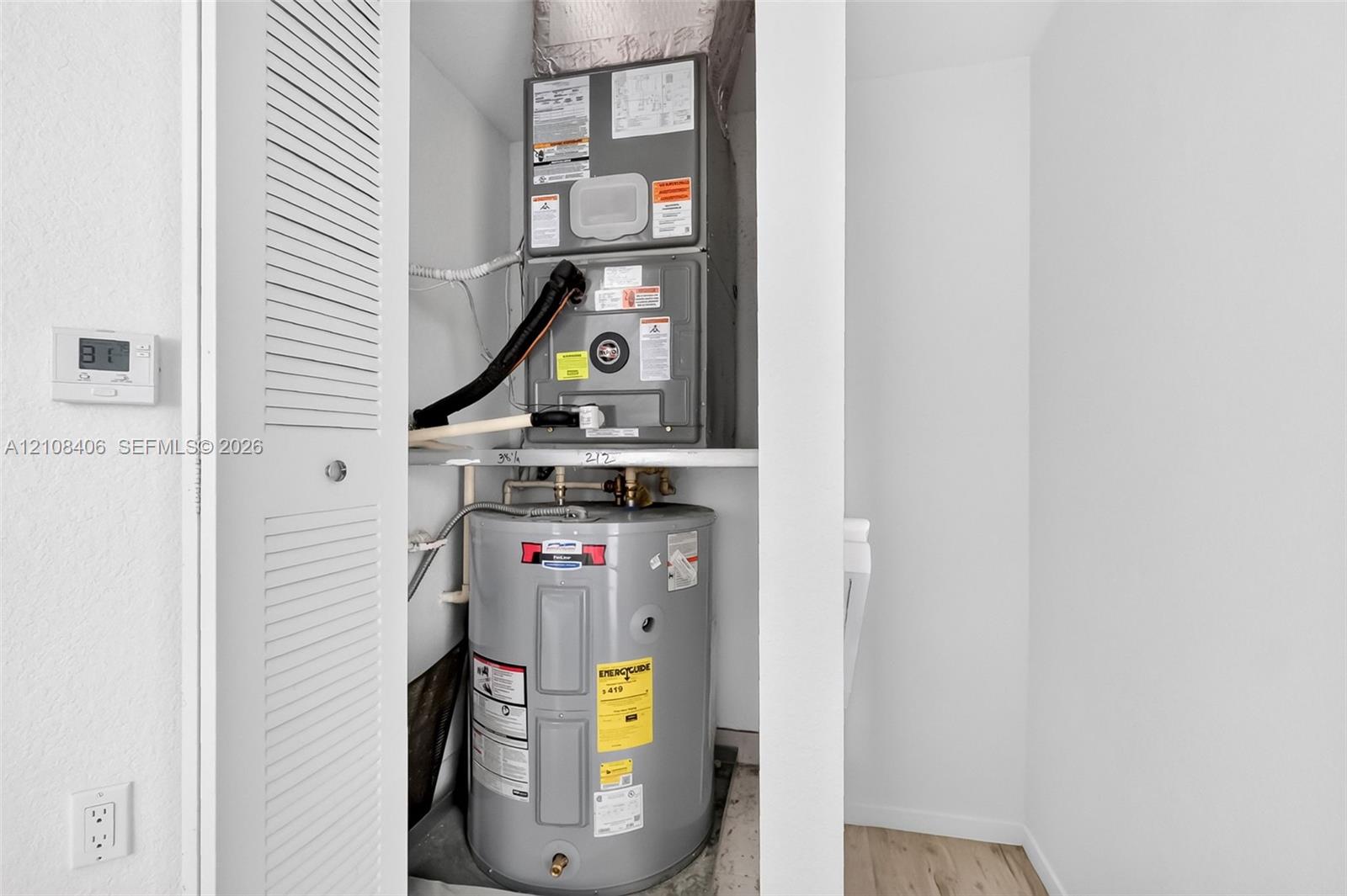 Utility closet featuring a stacked forced-air heating and cooling unit with an integrated water heater and louvered access door